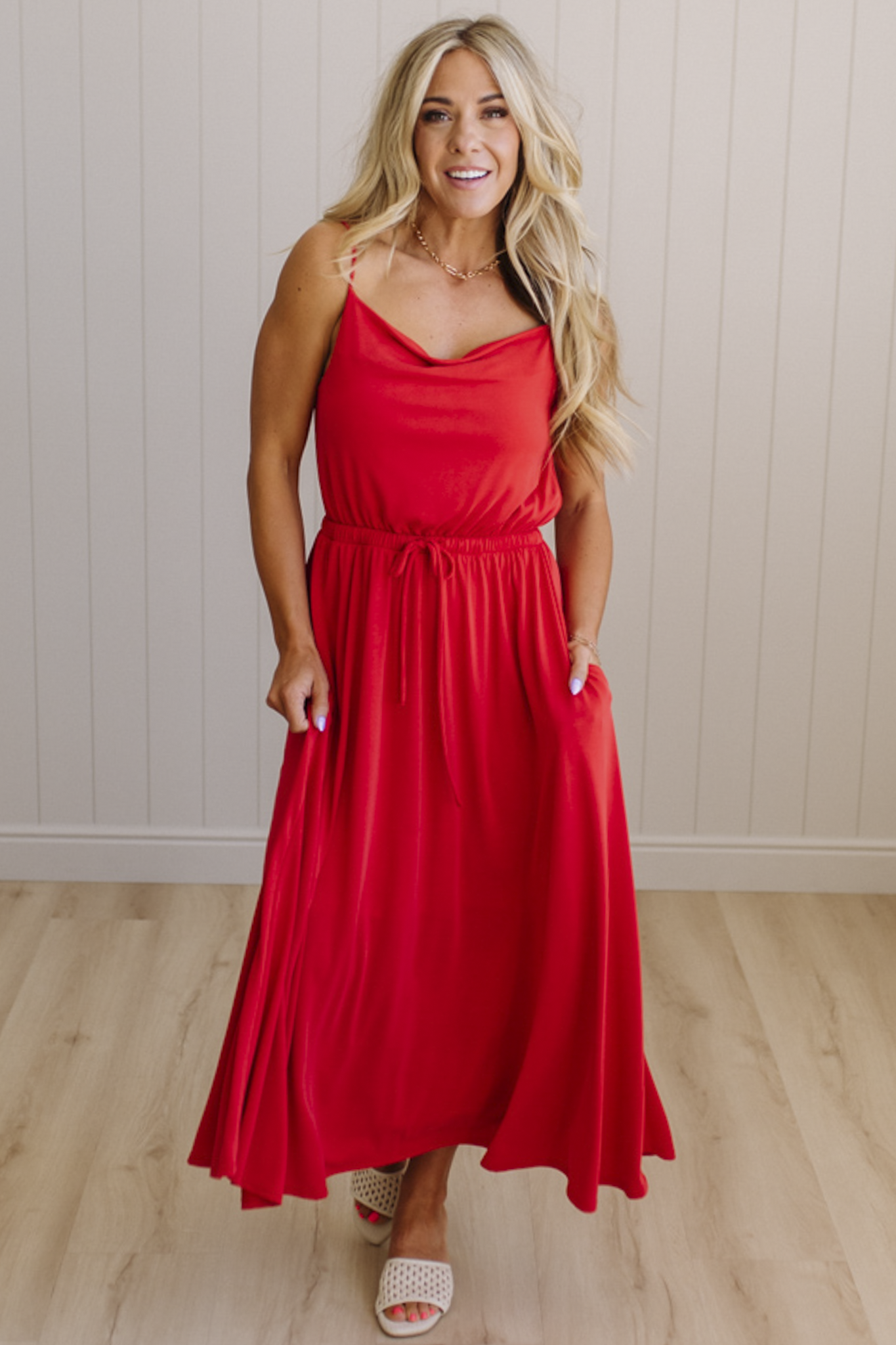 Woman wearing a red dress standing against a light wooden paneled wall.