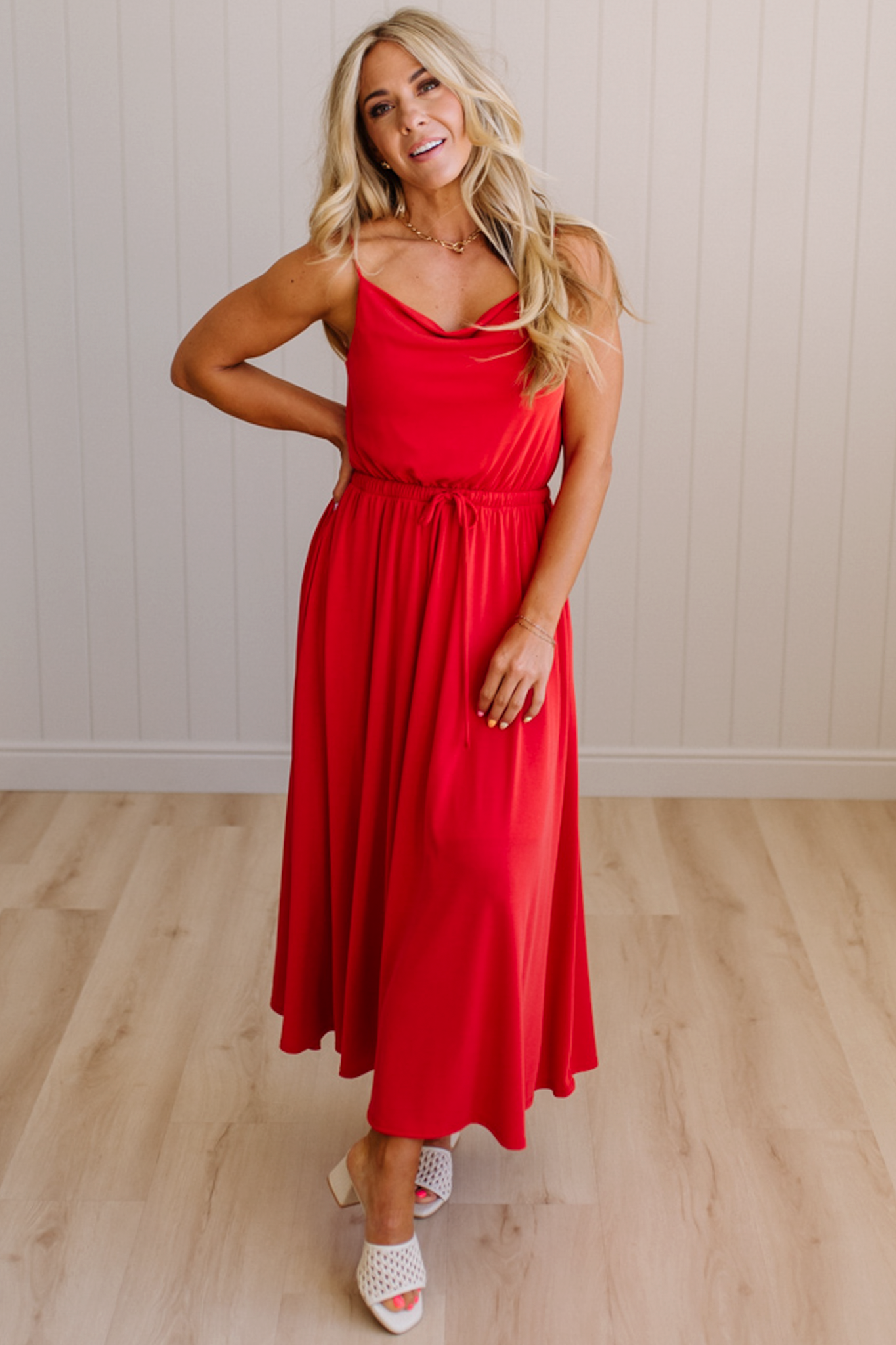 Woman wearing a red dress standing on a wooden floor with a white wall background