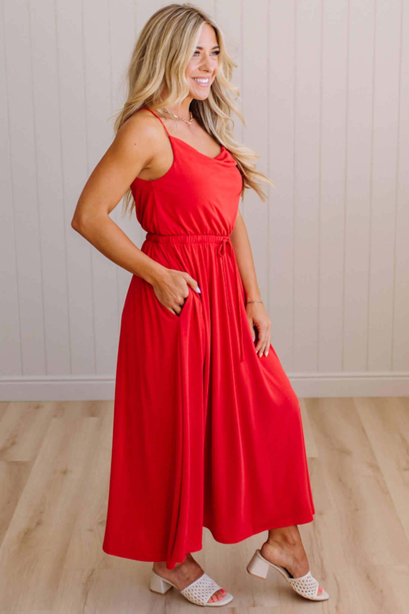 Woman wearing a red dress standing on a wooden floor with a white wall background