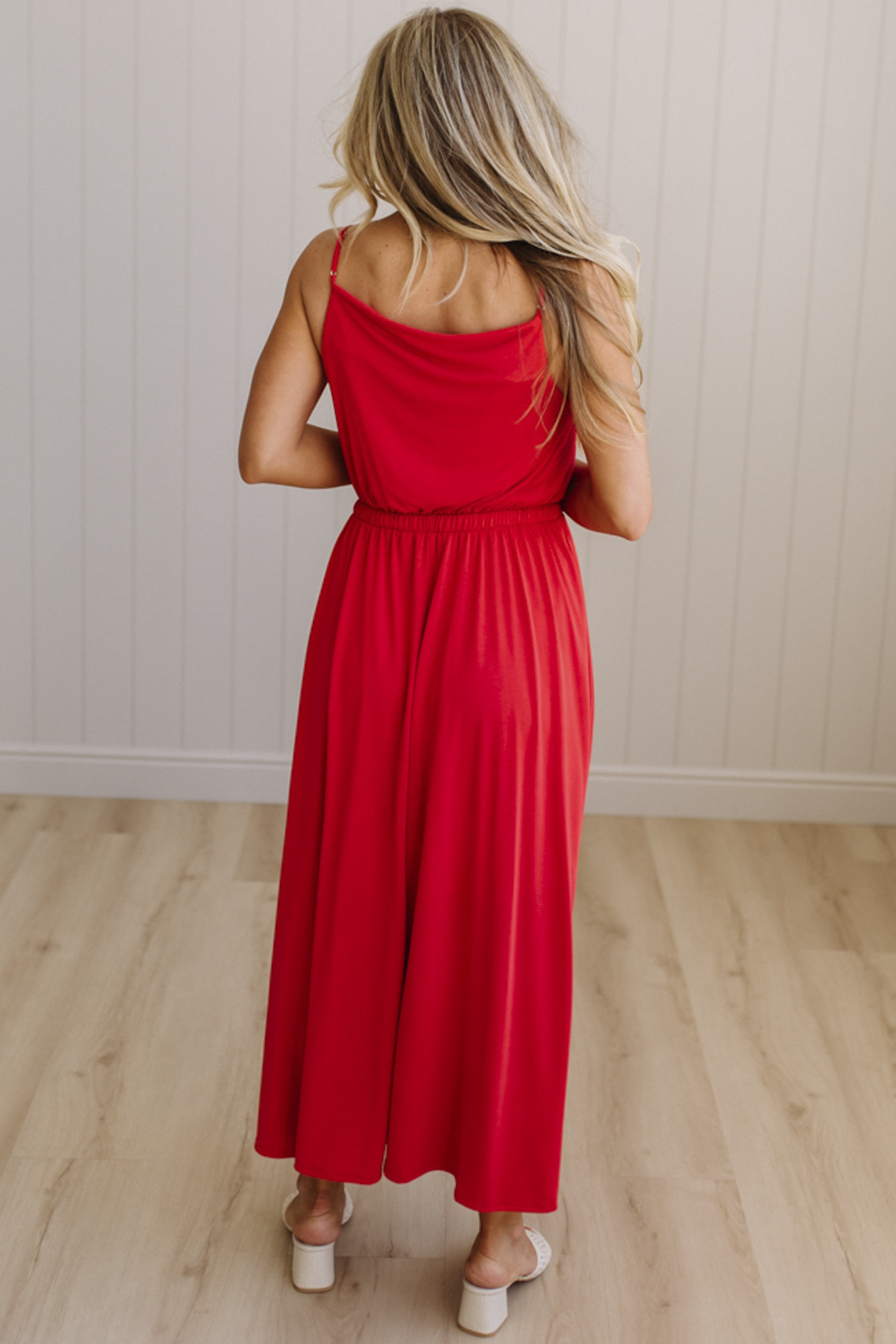 Woman wearing a red dress standing in a room with wooden flooring and a white wall.