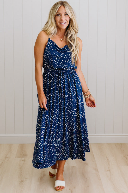 Woman wearing a blue polka dot dress standing against a white paneled wall.