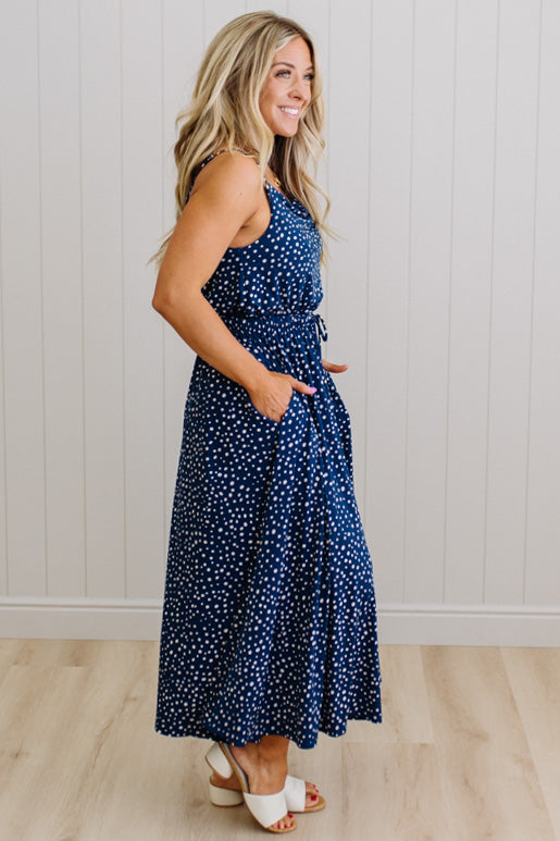 Woman wearing a blue polka dot dress standing against a white paneled wall.