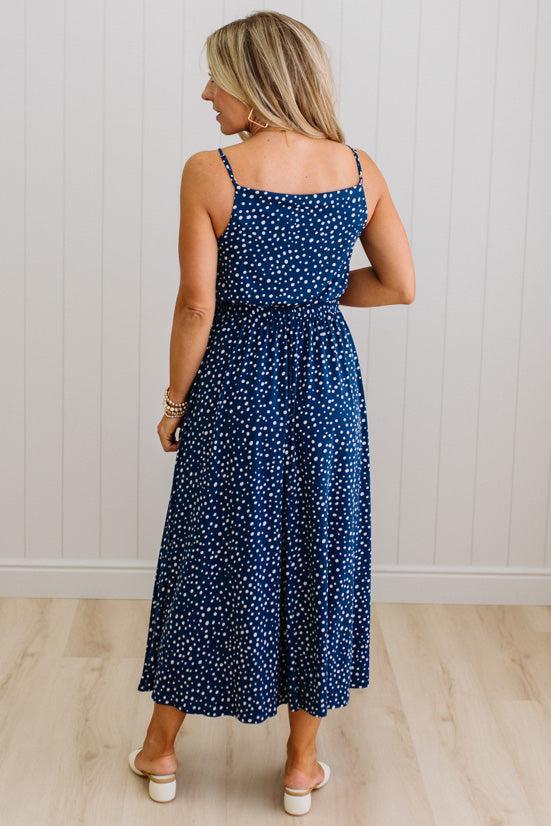 Woman wearing a blue polka dot dress standing against a white paneled wall.