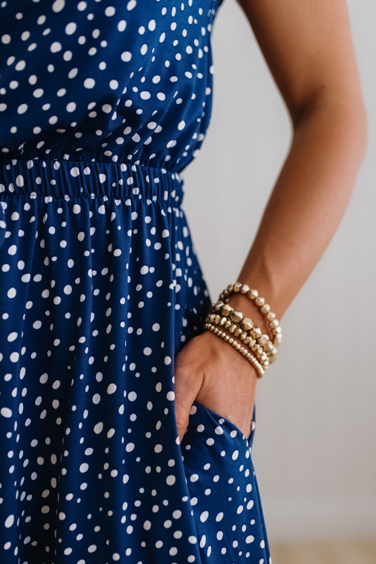 Person wearing a blue dress with white polka dots and gold bracelets on a neutral background