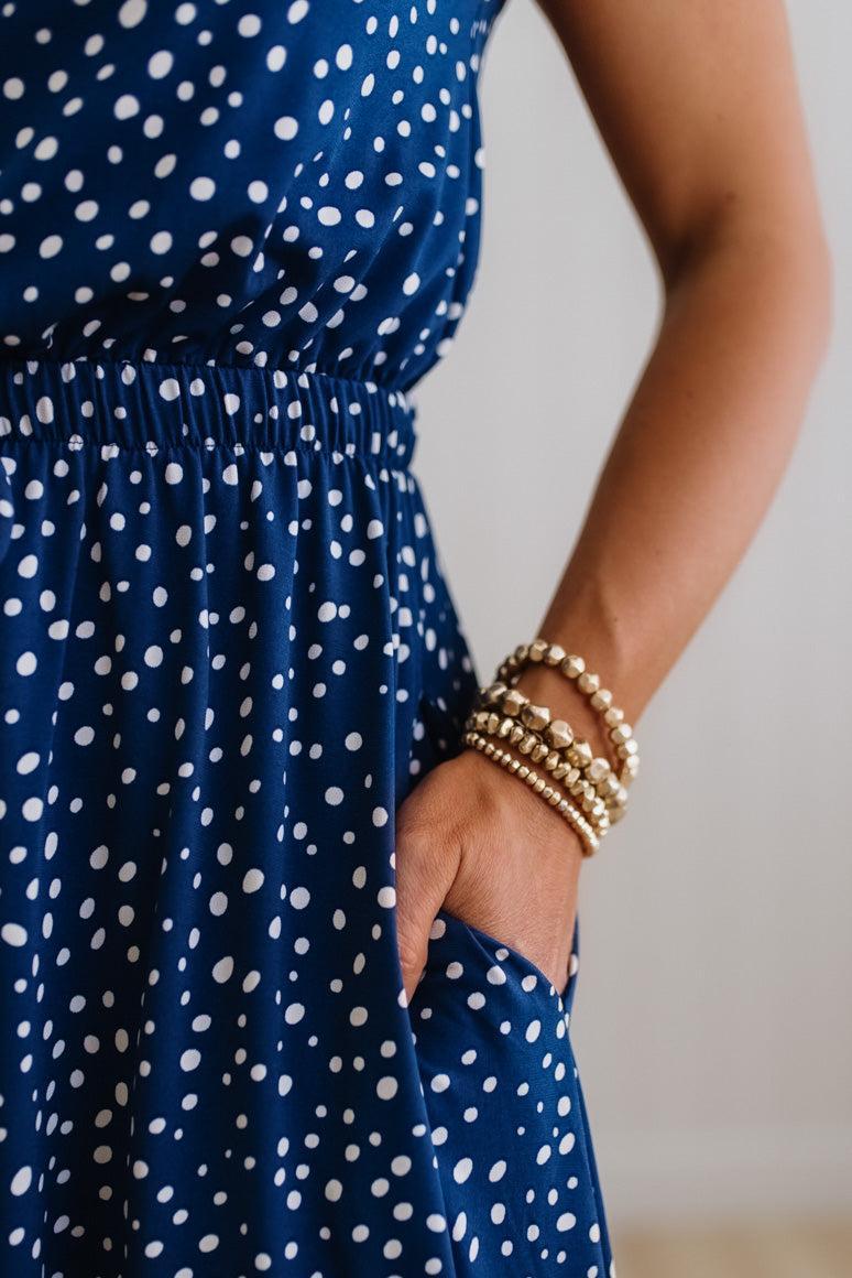 Person wearing a blue dress with white polka dots and gold bracelets on a neutral background
