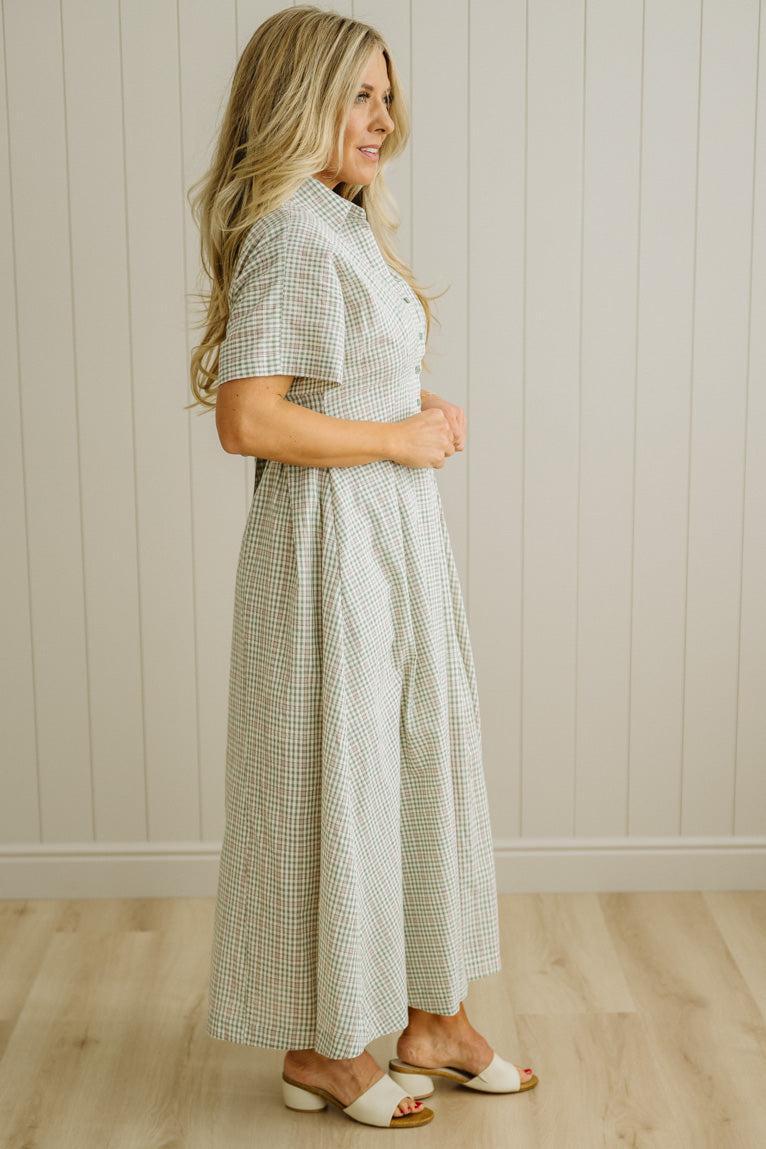 Woman wearing a checkered dress standing against a wooden paneled wall.