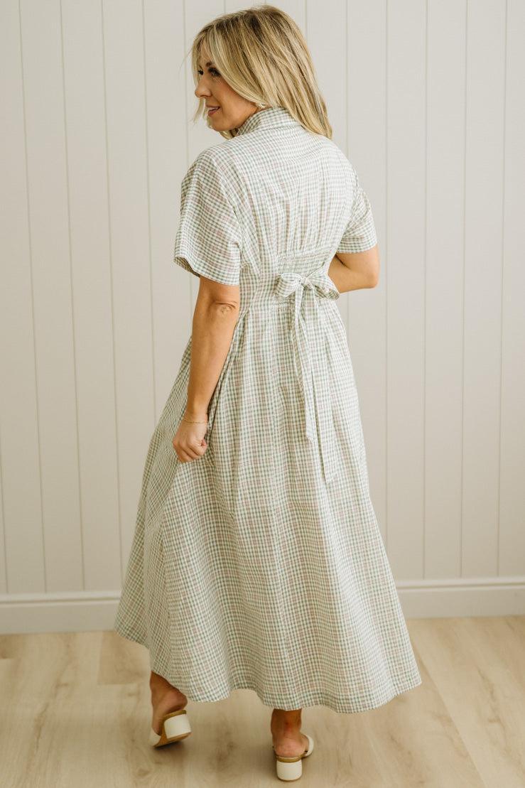 Woman wearing a checkered dress standing against a white paneled wall.