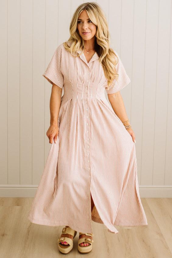 Woman wearing a pink striped dress standing against a white paneled wall.