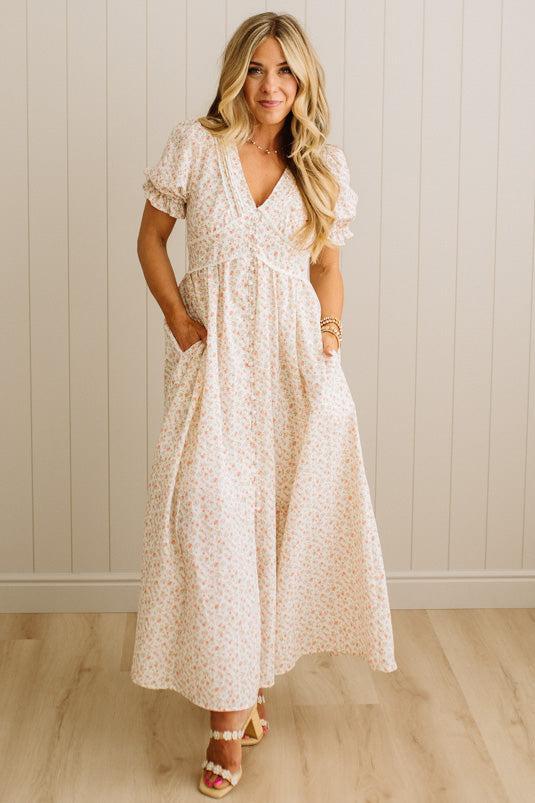 Woman wearing a floral dress standing against a white paneled wall.