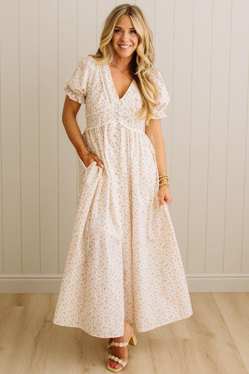 Woman wearing a floral dress against a light wooden paneled wall.