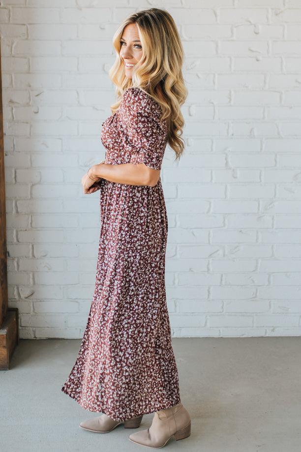 Woman wearing a floral dress standing against a white brick wall.