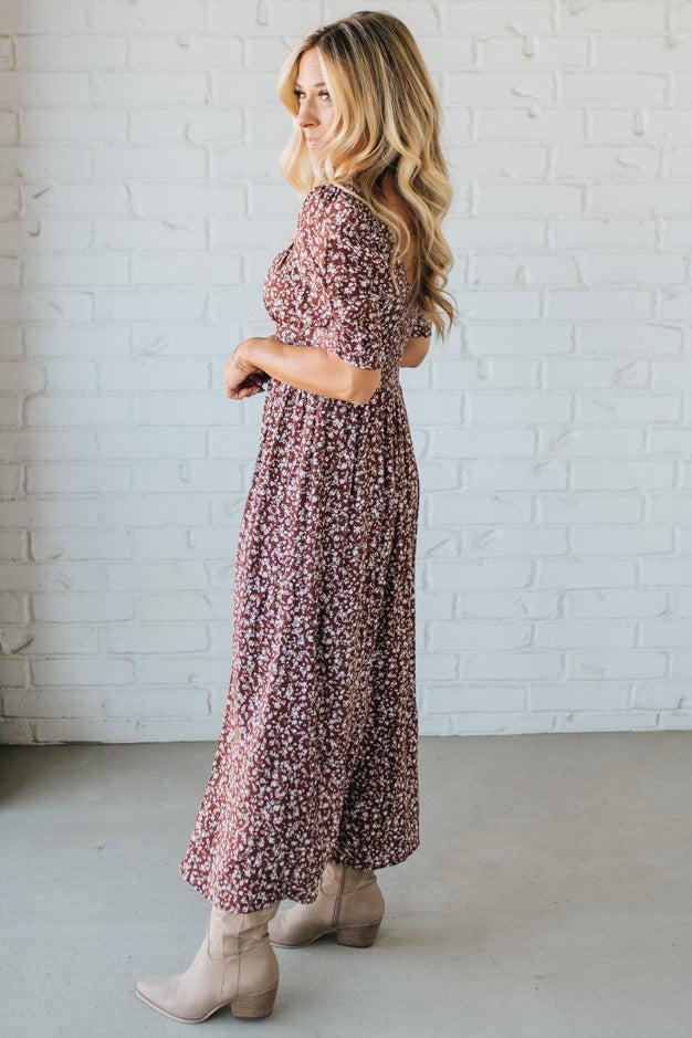 Woman wearing a floral dress standing against a white brick wall.