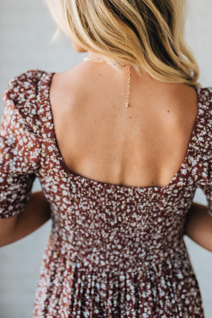 Woman wearing a floral dress with a backless design, standing against a neutral background.