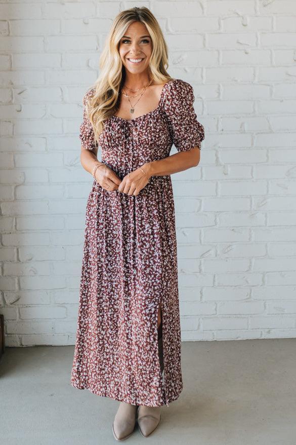 Woman wearing a floral dress against a white brick wall.