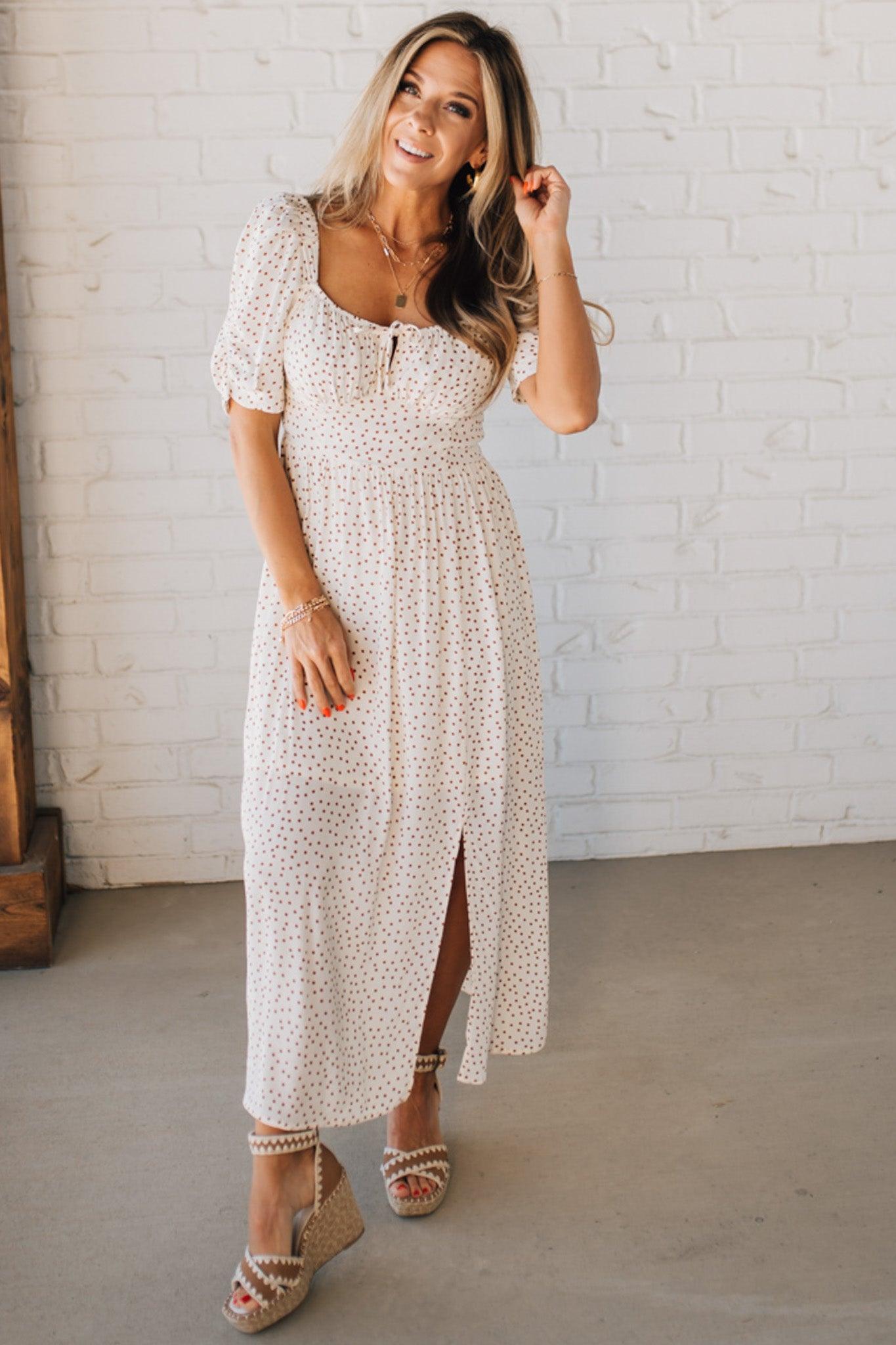 BLONDE WOMAN WEARING A CAMEL DOT PRINT CREAM MAXI DRESS W/ RUCHED BODICE & SLEEVES AND SIDE SLIT