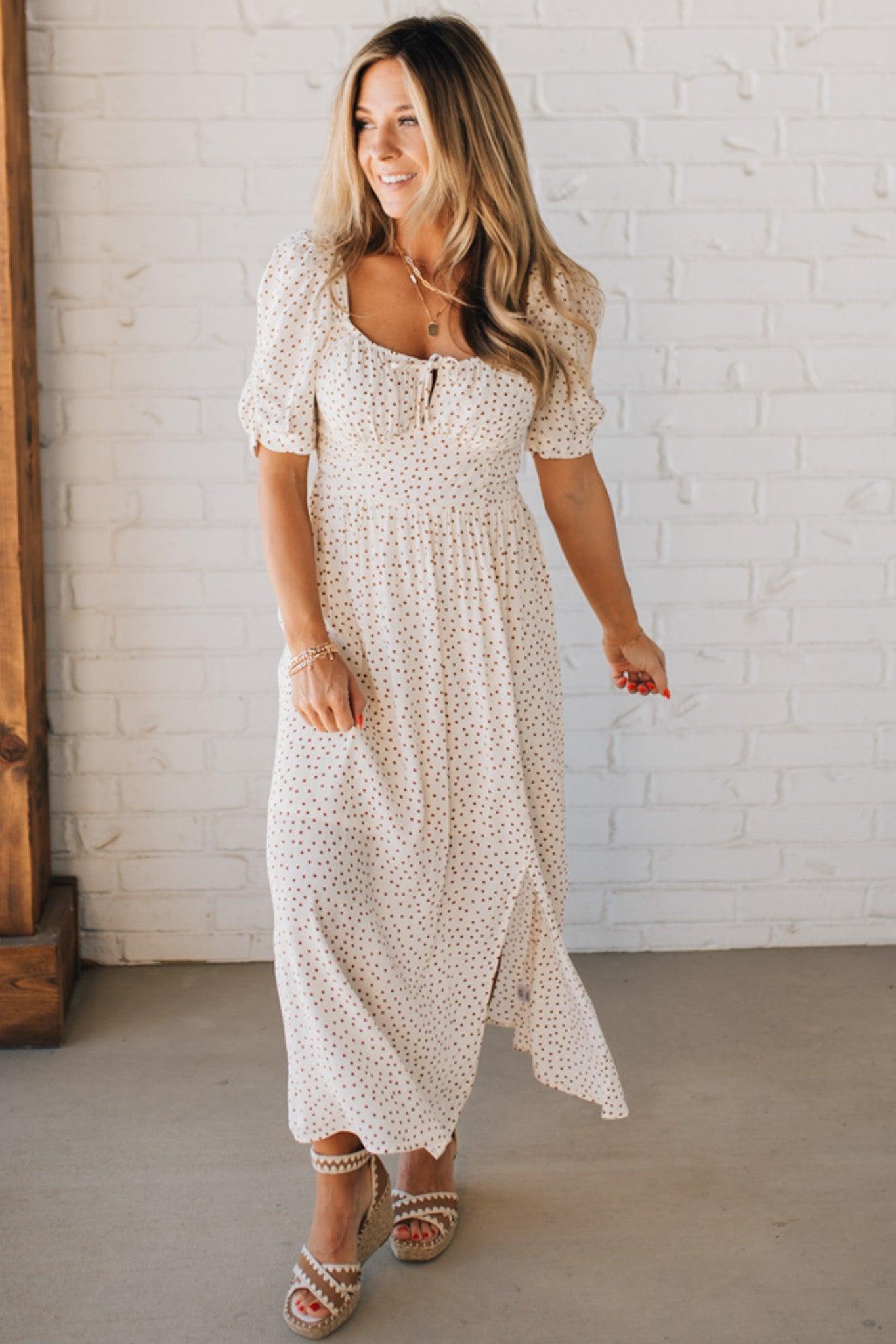 BLONDE WOMAN WEARING A CAMEL DOT PRINT CREAM MAXI DRESS W/ RUCHED BODICE & SLEEVES AND SIDE SLIT