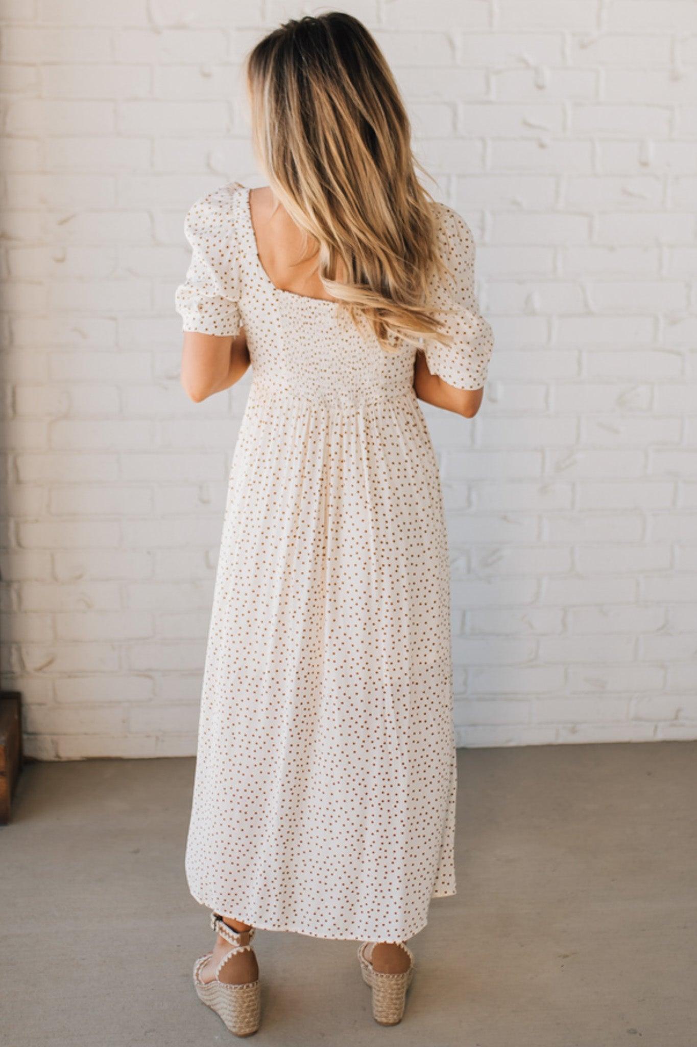 BLONDE WOMAN WEARING A CAMEL DOT PRINT CREAM MAXI DRESS W/ RUCHED BODICE & SLEEVES AND SIDE SLIT