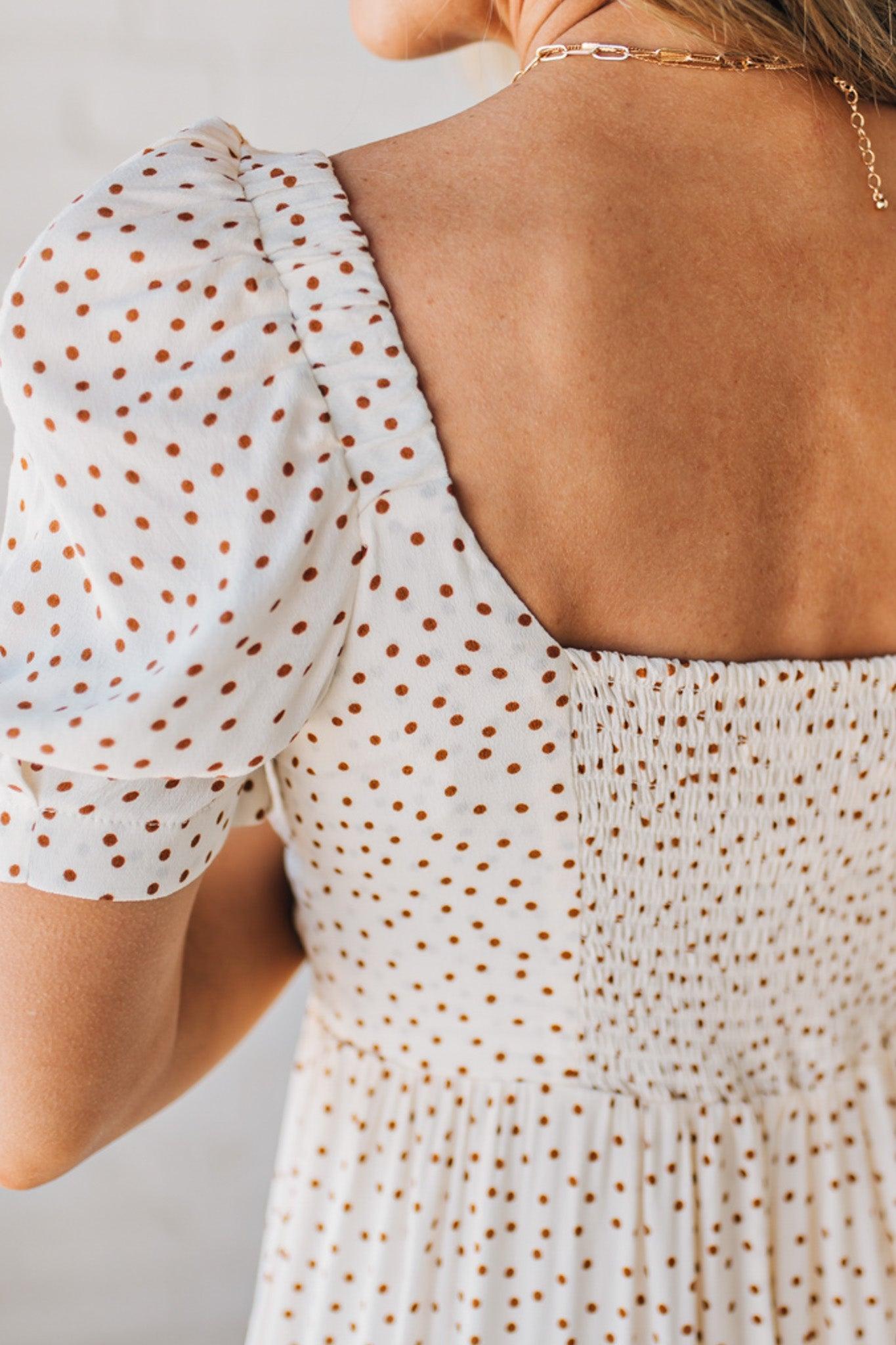 BLONDE WOMAN WEARING A CAMEL DOT PRINT CREAM MAXI DRESS W/ RUCHED BODICE & SLEEVES AND SIDE SLIT