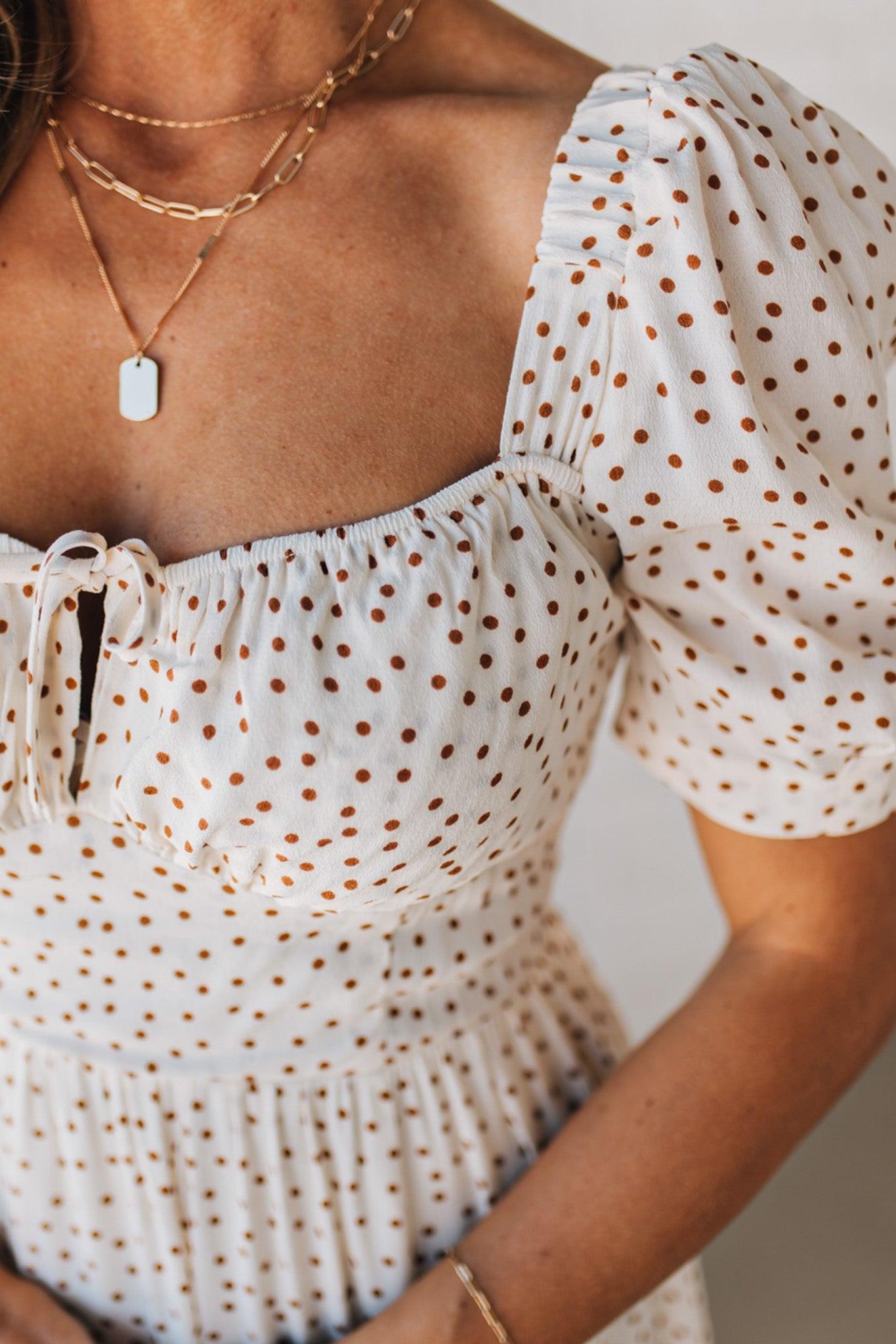 BLONDE WOMAN WEARING A CAMEL DOT PRINT CREAM MAXI DRESS W/ RUCHED BODICE & SLEEVES AND SIDE SLIT