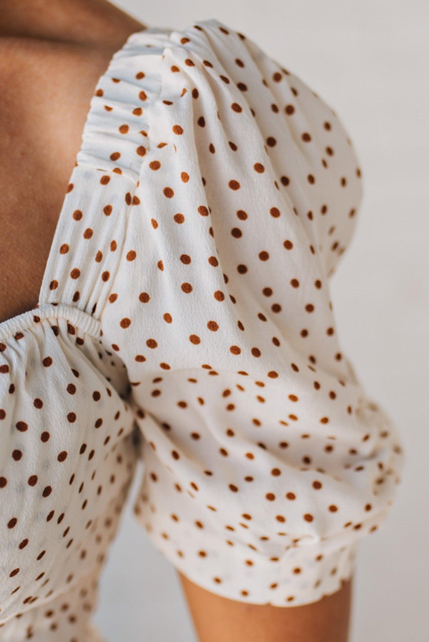 BLONDE WOMAN WEARING A CAMEL DOT PRINT CREAM MAXI DRESS W/ RUCHED BODICE & SLEEVES AND SIDE SLIT