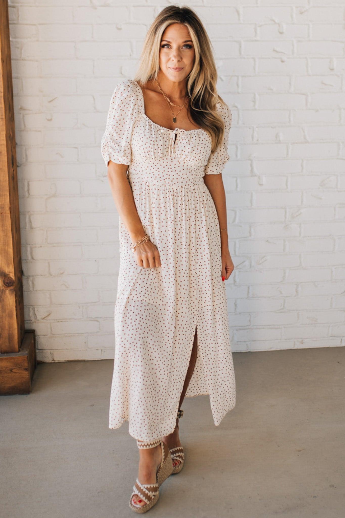 BLONDE WOMAN WEARING A CAMEL DOT PRINT CREAM MAXI DRESS W/ RUCHED BODICE & SLEEVES AND SIDE SLIT