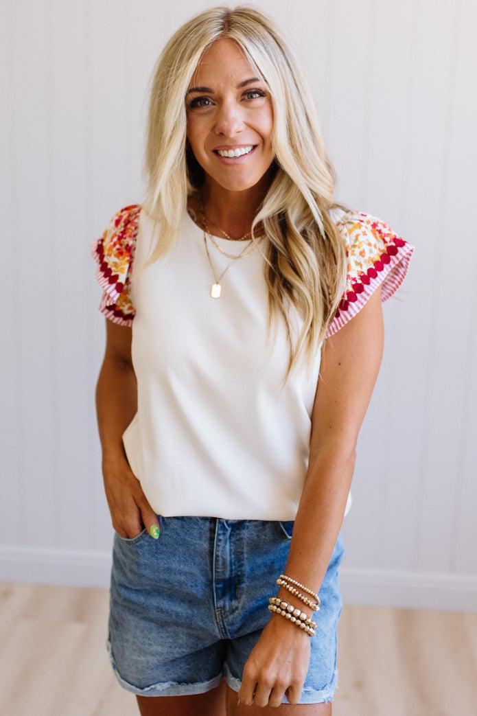 Woman wearing a white top with colorful sleeves and denim shorts against a plain background