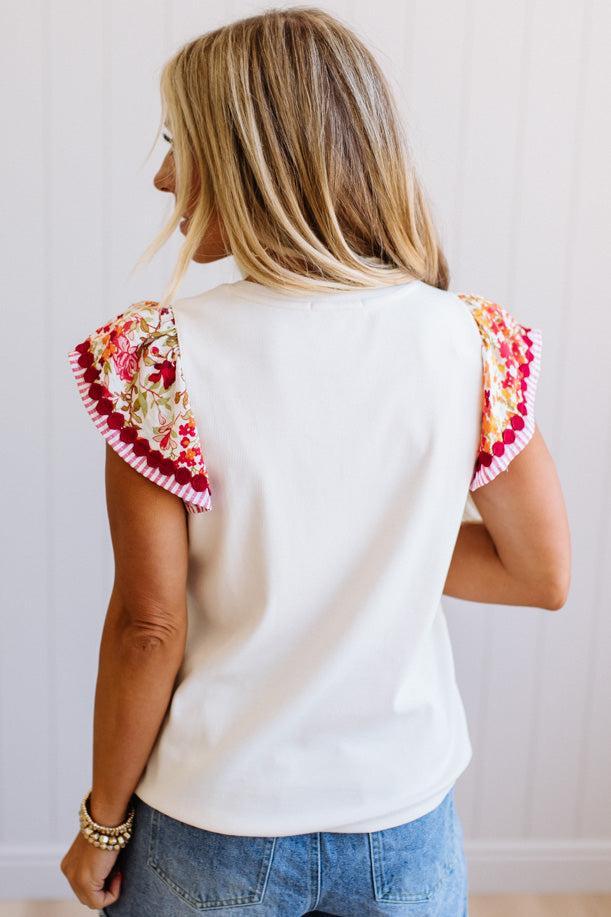 Woman wearing a white sleeveless top with colorful floral sleeves against a plain background