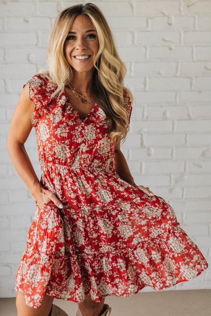 Woman wearing a red floral dress against a white brick wall.