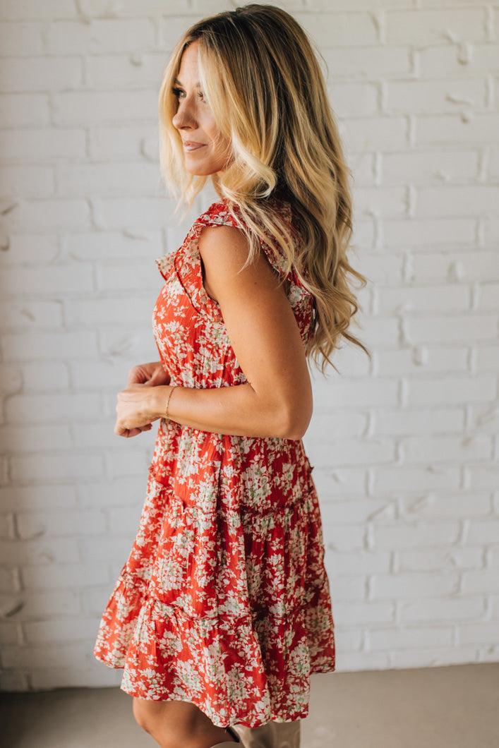 Woman wearing a red floral dress against a white brick wall.
