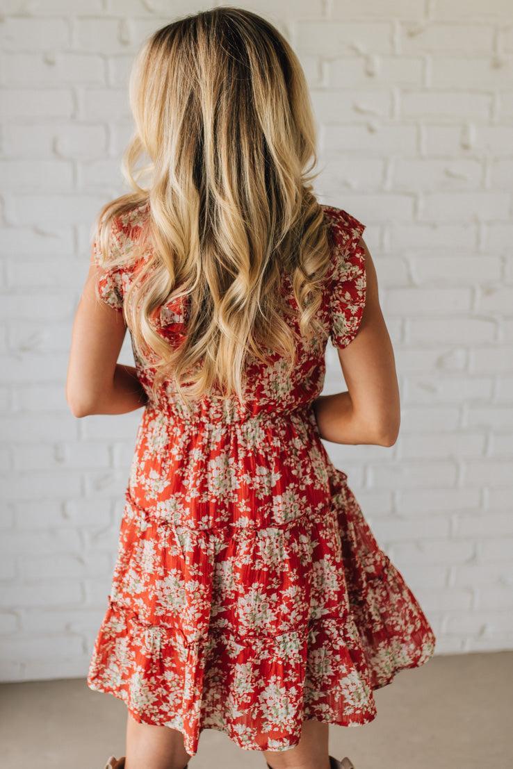 Woman wearing a red floral dress against a white brick wall.