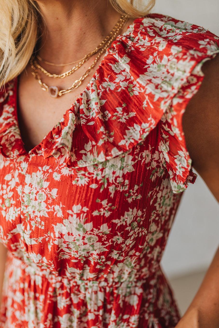 Red floral dress with gold necklaces on a blurred background