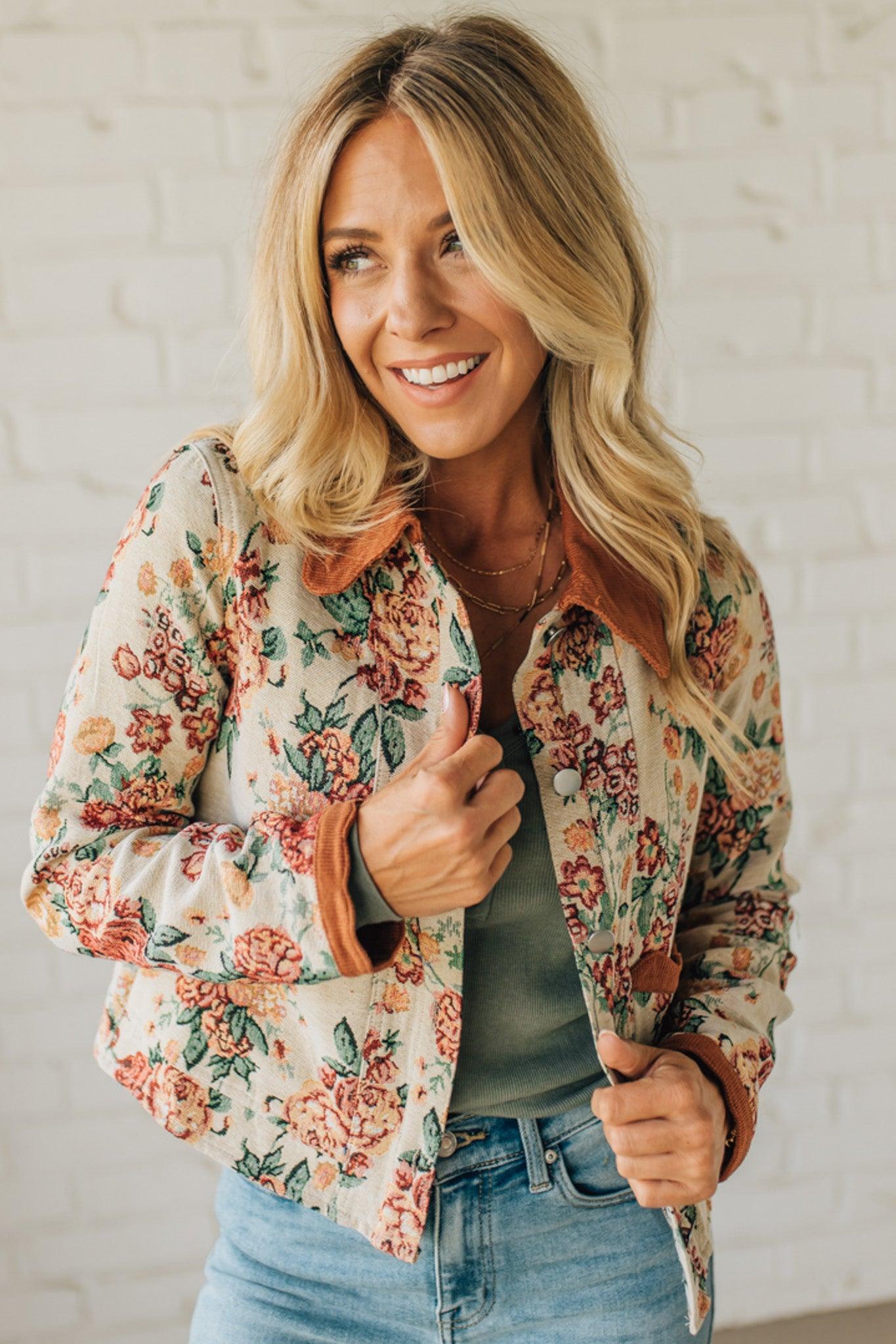 Woman wearing a floral jacket and smiling against a white brick wall.