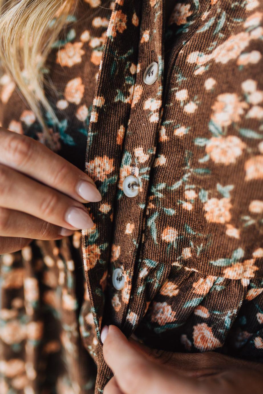 Close-up of a brown floral dress with buttons being adjusted by hands.