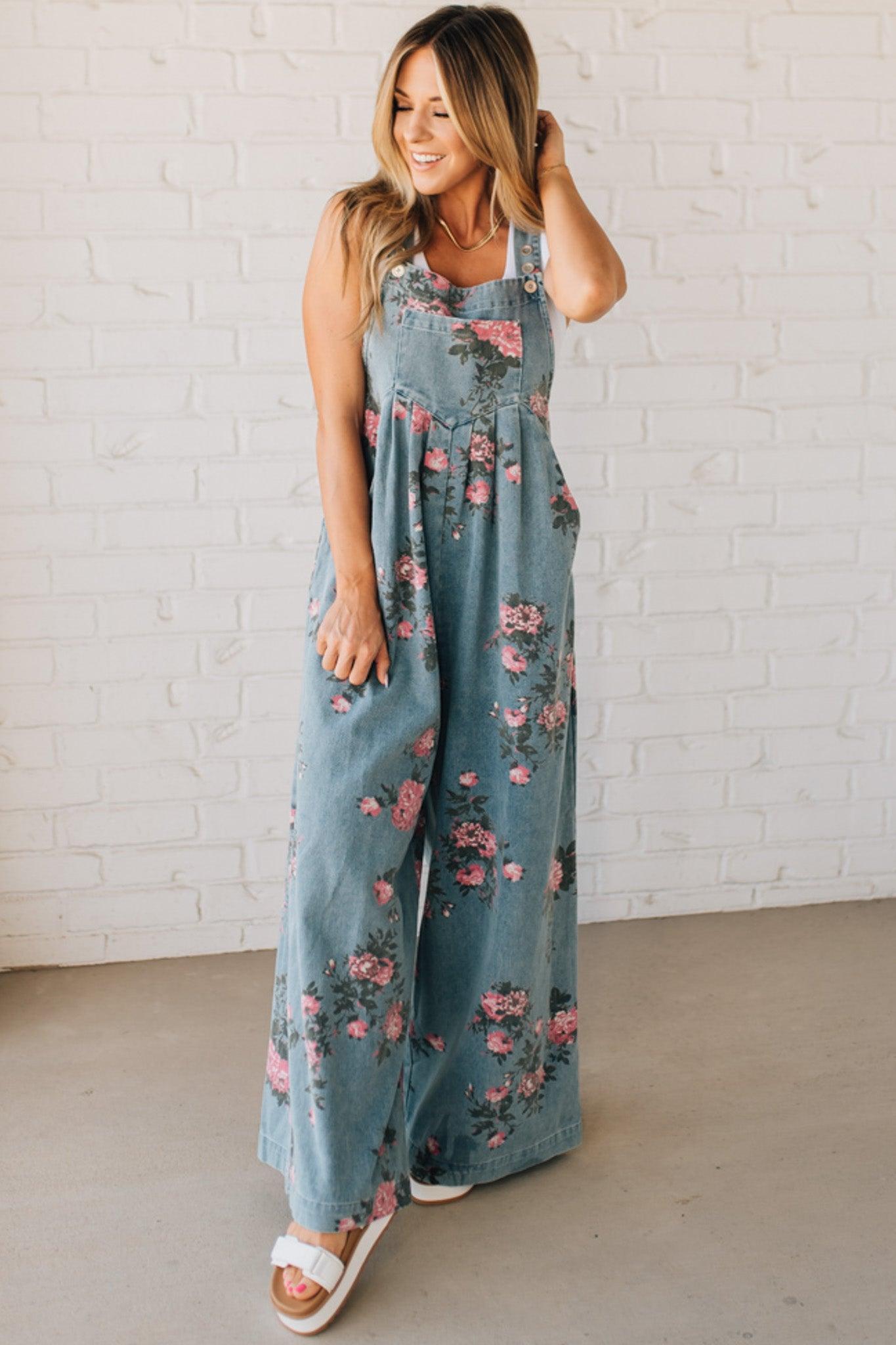 BLONDE WOMAN WEARING FLOWER PRINT WASHED DENIM WIDE LEG OVERALLS WITH ADJUSTABLE BUTTONED SHOULDER STRAP.