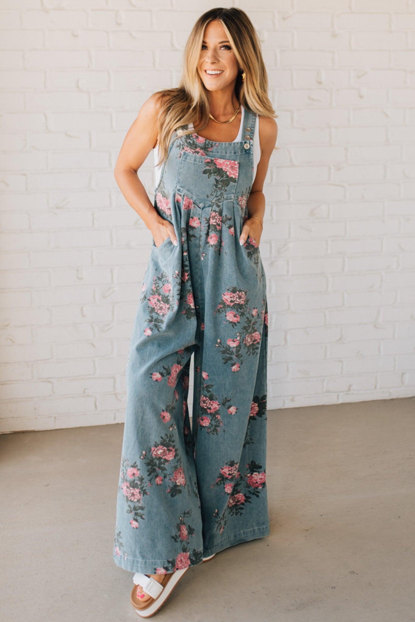 BLONDE WOMAN WEARING FLOWER PRINT WASHED DENIM WIDE LEG OVERALLS WITH ADJUSTABLE BUTTONED SHOULDER STRAP.
