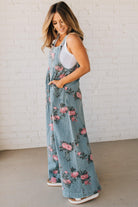 BLONDE WOMAN WEARING FLOWER PRINT WASHED DENIM WIDE LEG OVERALLS WITH ADJUSTABLE BUTTONED SHOULDER STRAP.