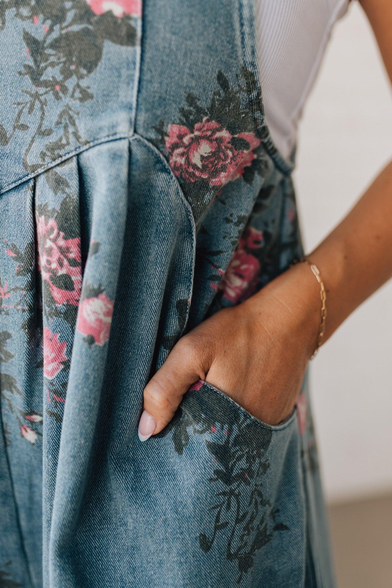 BLONDE WOMAN WEARING FLOWER PRINT WASHED DENIM WIDE LEG OVERALLS WITH ADJUSTABLE BUTTONED SHOULDER STRAP.
