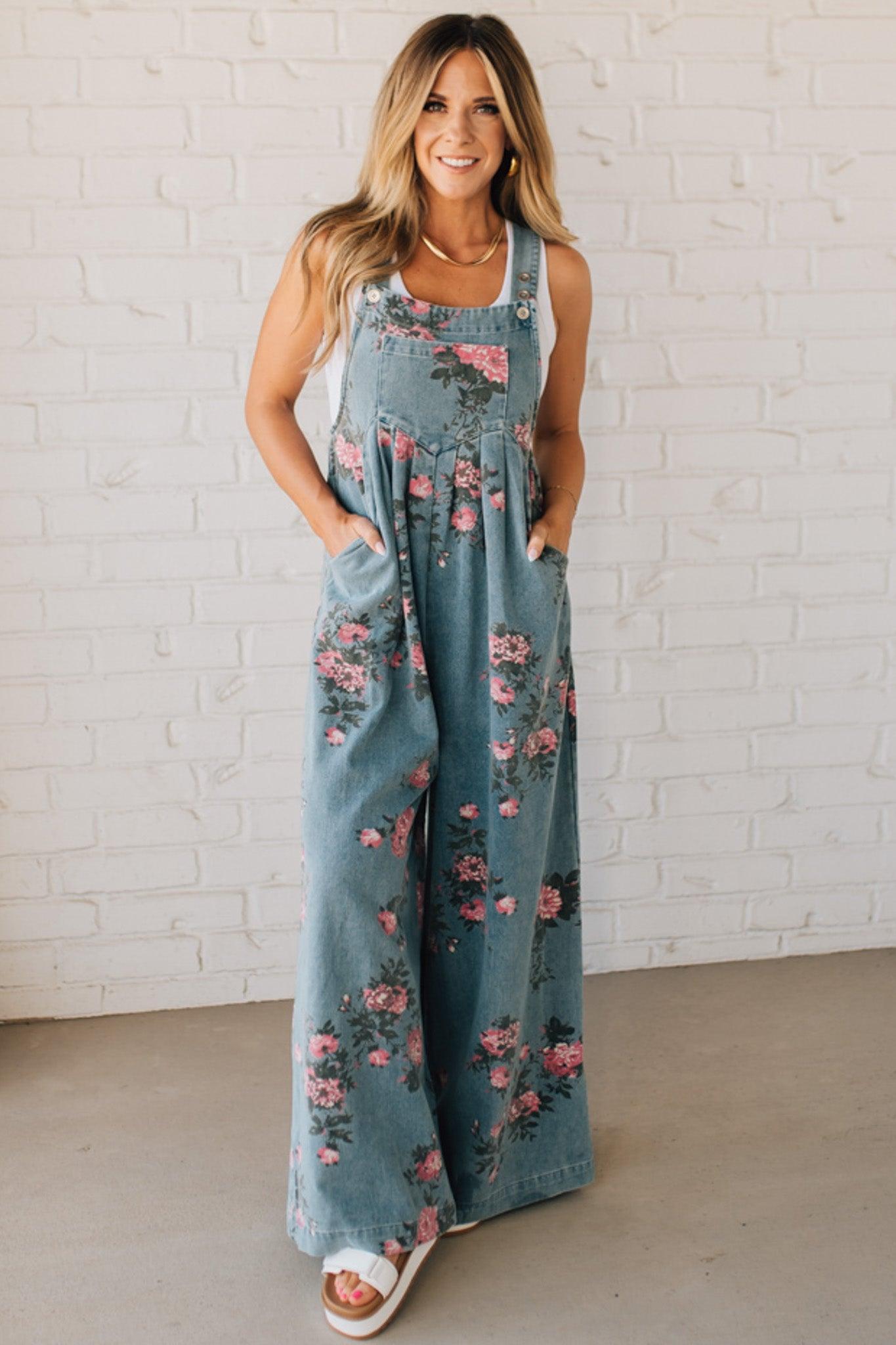 BLONDE WOMAN WEARING FLOWER PRINT WASHED DENIM WIDE LEG OVERALLS WITH ADJUSTABLE BUTTONED SHOULDER STRAP.