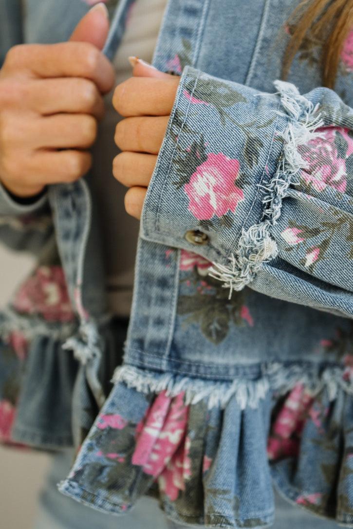 Close-up of a denim jacket with floral patterns and ruffled details.