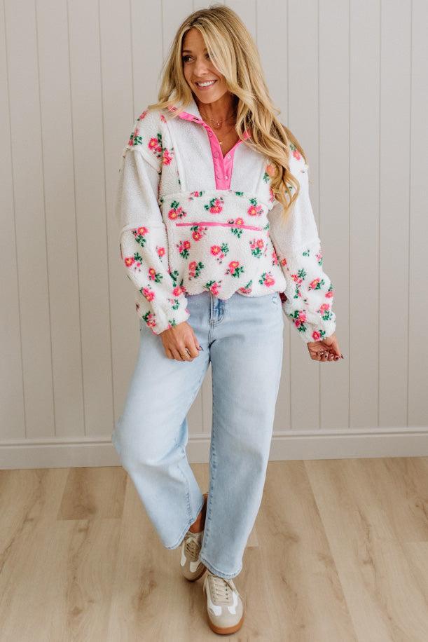 Woman wearing a floral hoodie and light blue jeans indoors.