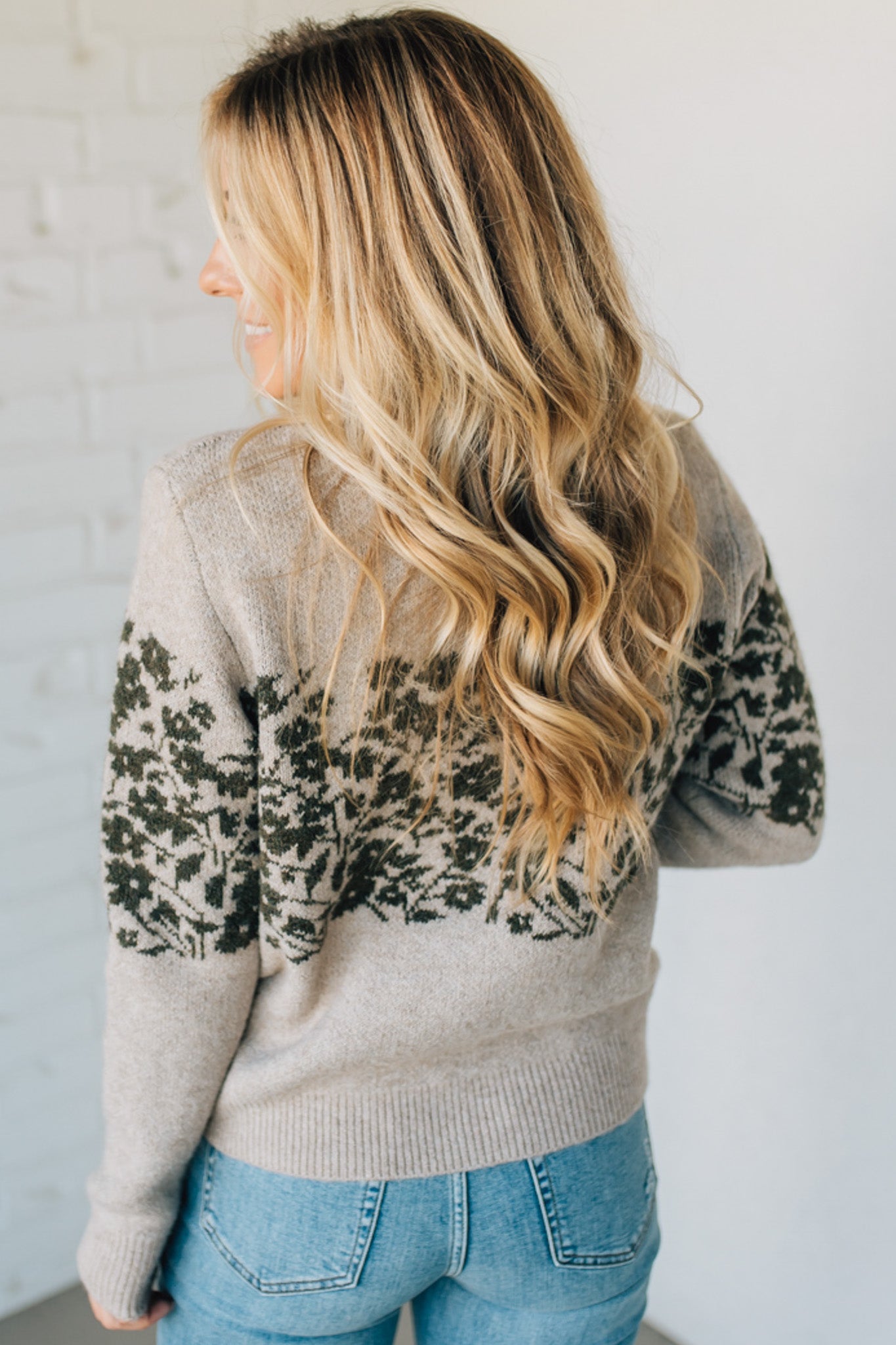 Person wearing a beige sweater with floral patterns, standing against a plain background