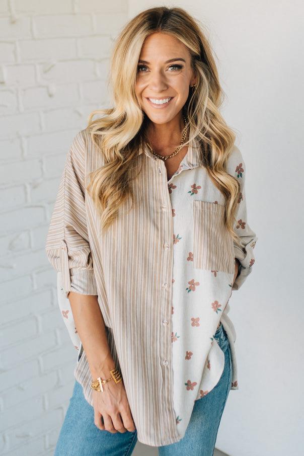 Woman wearing a layered outfit with a striped shirt over a floral top against a white brick wall.