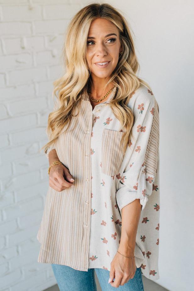 Woman wearing a floral blouse over a striped shirt against a white brick wall.