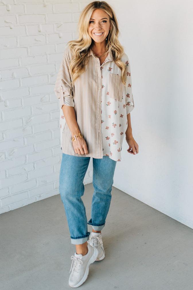 Woman wearing a striped shirt, floral blouse, blue jeans, and white sneakers against a white brick wall.