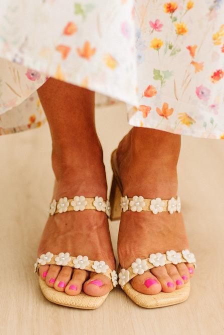 Brown sandals with floral embellishments worn with a floral dress on a neutral background