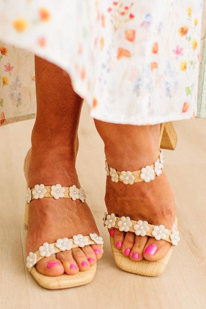 Close-up of feet wearing beige sandals with white floral straps on a neutral background