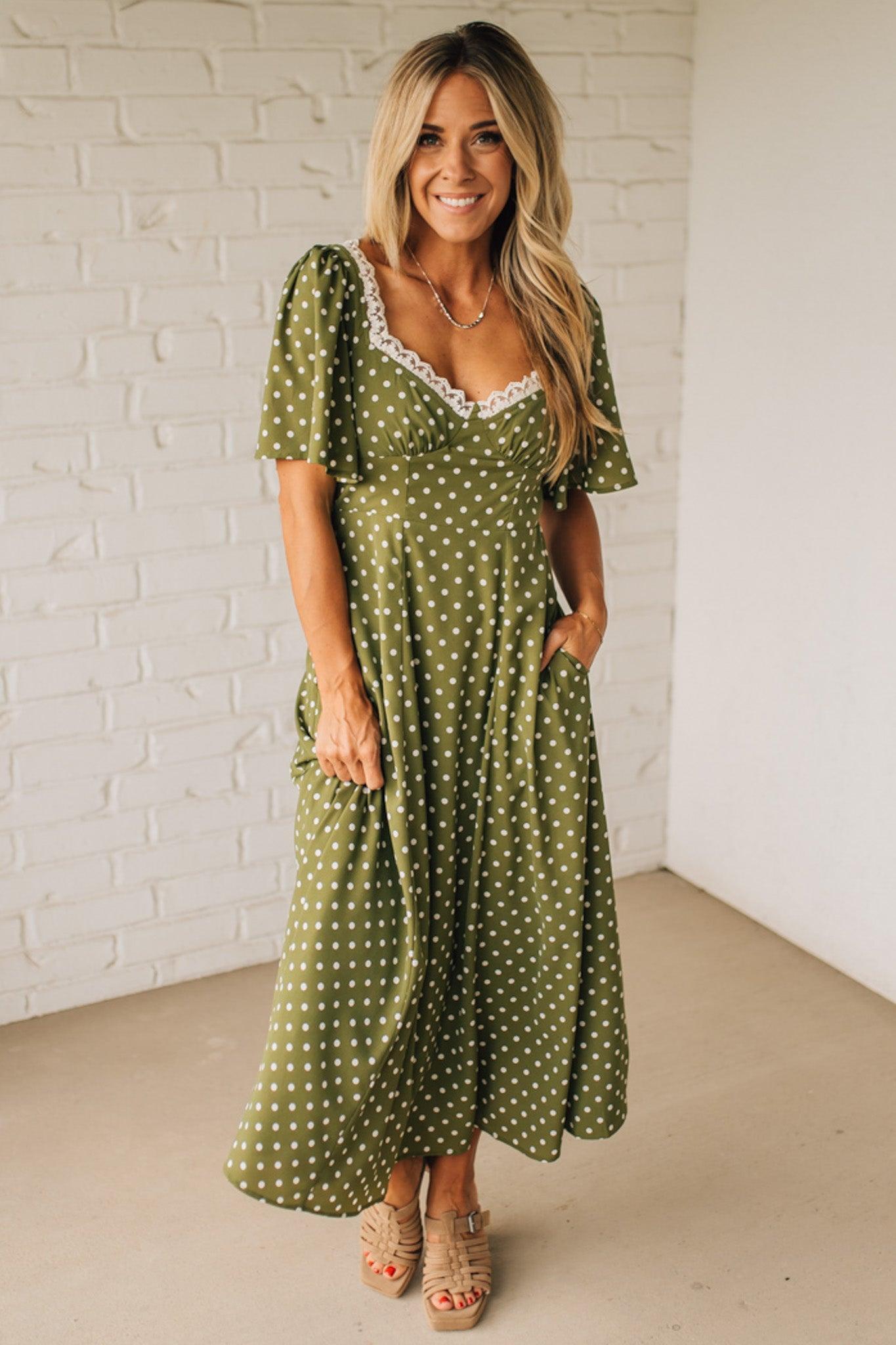Woman wearing a green polka dot dress against a white brick wall.