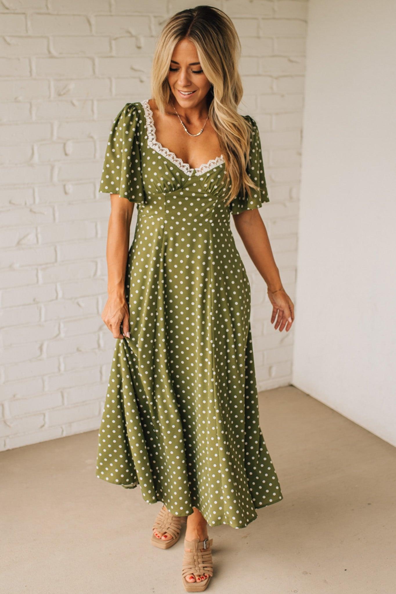 Woman wearing a green polka dot dress against a white brick wall.