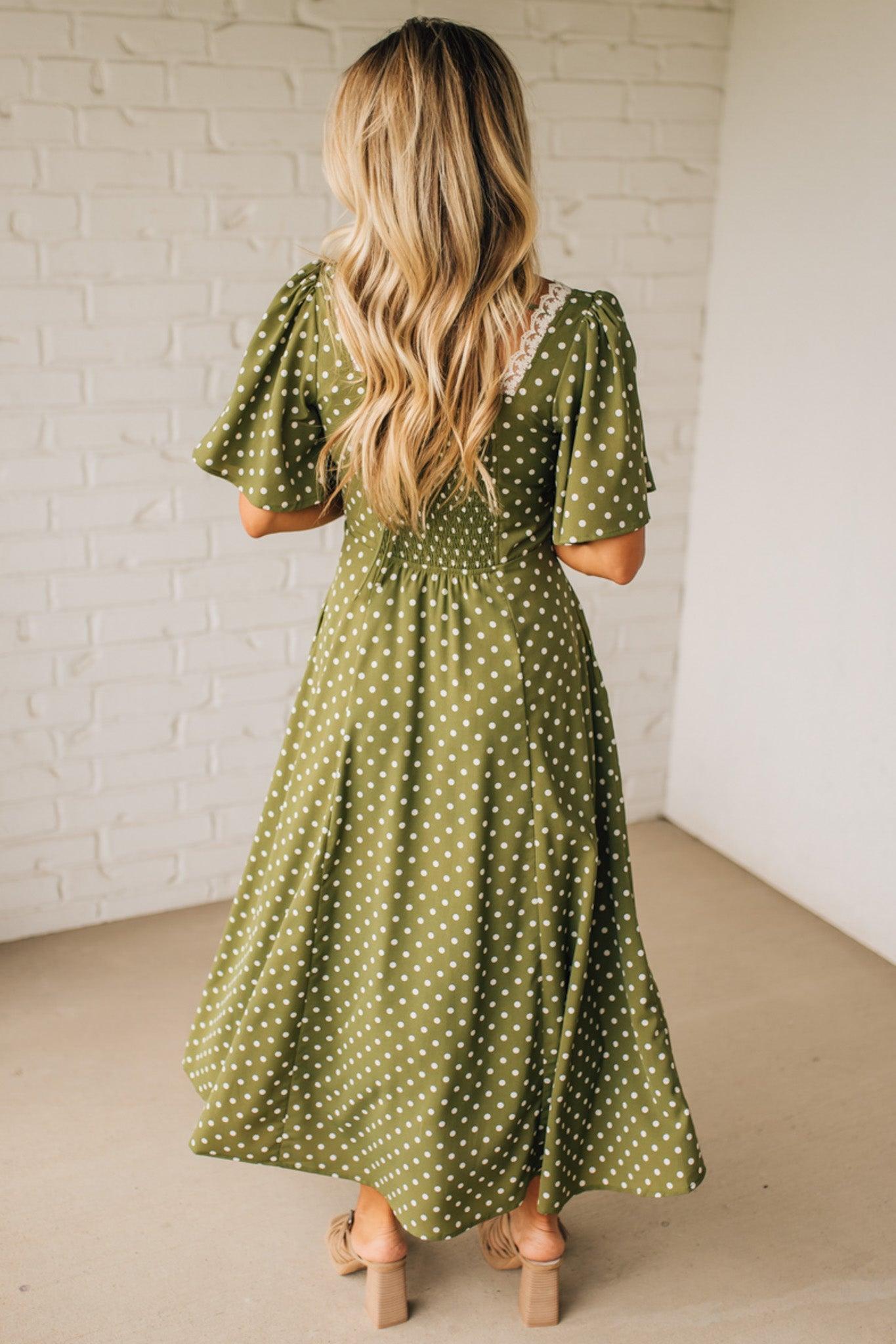 Woman wearing a green polka dot dress standing against a white brick wall.