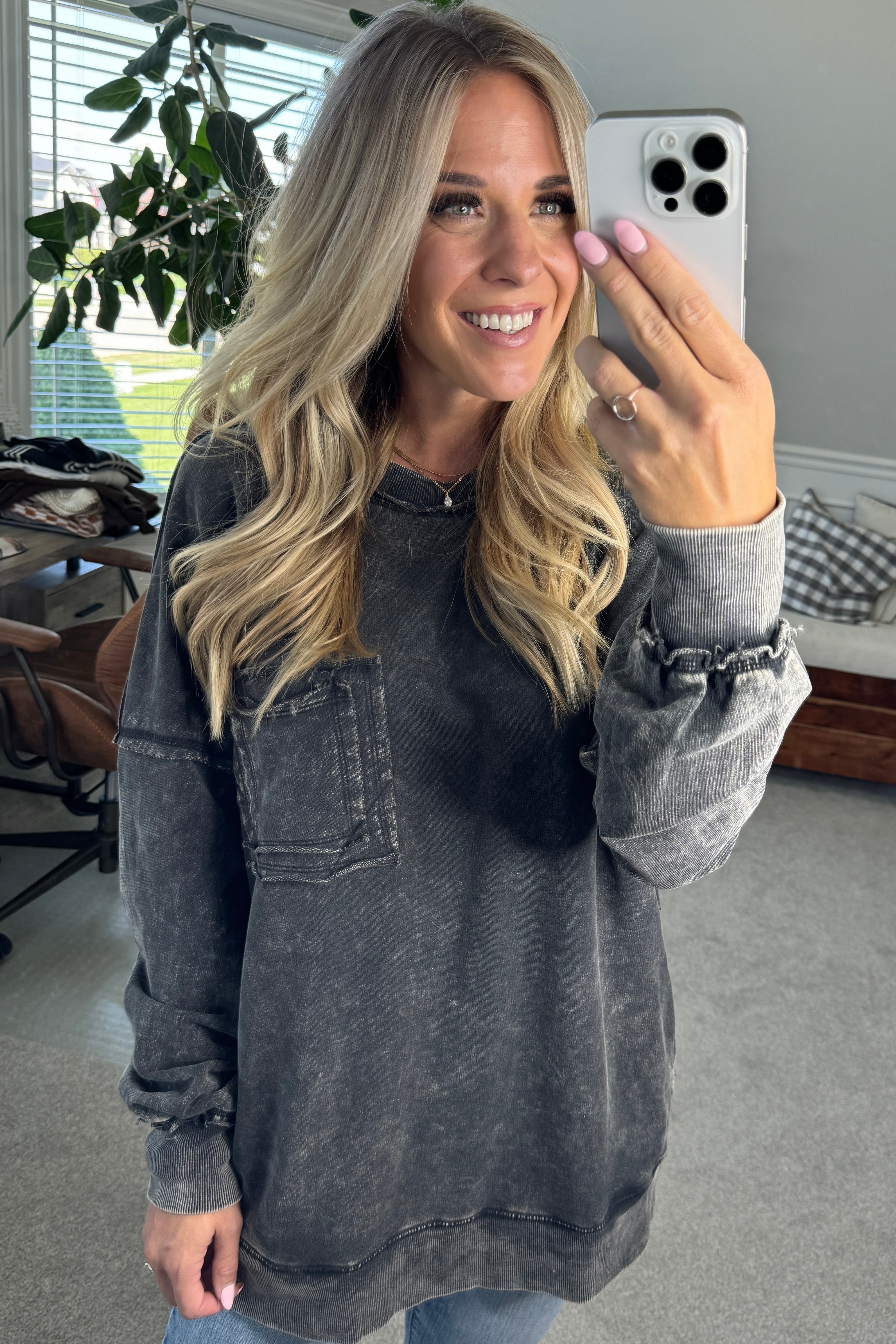Blonde woman wearing a boyfriend fit drop shoulder sweatshirt pullover, with front pocket accent, exposed raw seams, and all over acid wash detail.